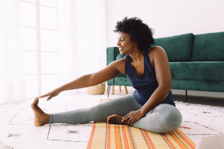 African woman doing exercise at home. Mature woman doing stretching workout in living room.