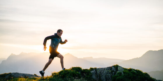 Young man runs on mountain ridge at sunrise